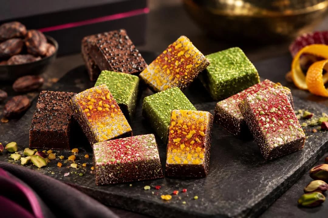 Art Range bonbons in red, gold, green and dark decorated finishes on slate, with pistachios and orange peel